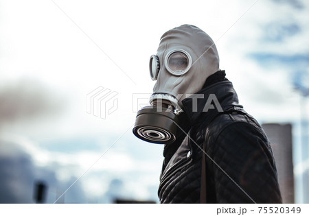 casual young man in a gas mask standing on the street in an empty city 75520349