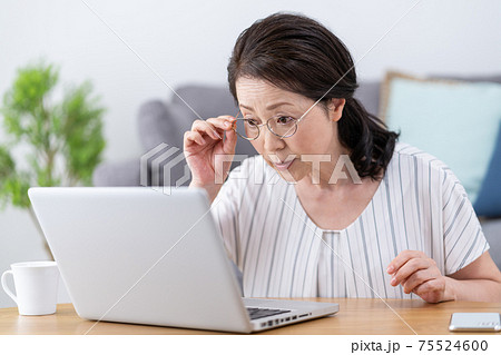 老眼　画面がよく見えずに老眼鏡をかけてパソコンを見るシニア女性 75524600