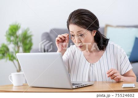 老眼　画面がよく見えずに老眼鏡をかけてパソコンを見るシニア女性 75524602