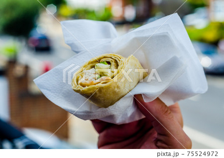 Chicken breast with caesar dressing and lettuce in a gluten-free tortilla wrap in the hand 75524972