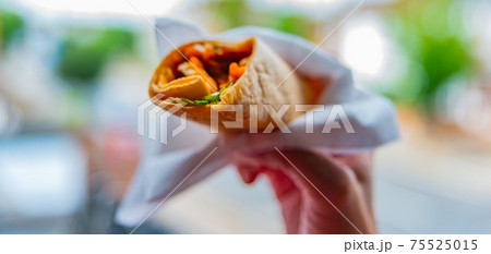 Chicken breast with piri piri sauce and lettuce in a chili tortilla wrap in the hand 75525015