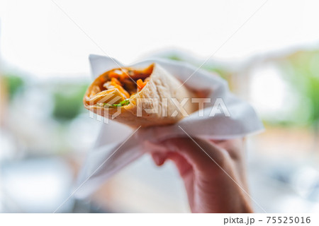Chicken breast with piri piri sauce and lettuce in a chili tortilla wrap in the hand 75525016