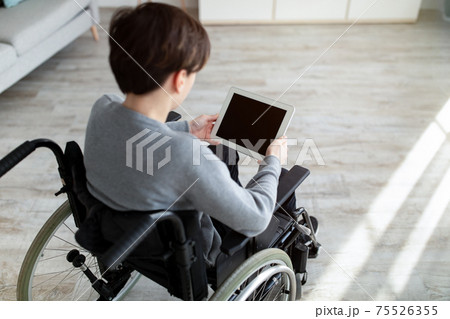 Handicapped teenage boy in wheelchair holding tablet with blank screen indoors, mockup for website or app design 75526355