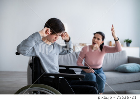 Teenage boy in wheelchair having fight with his angry mom, closing ears not to hear her quarreling at home Teenage boy in wheelchair having fight with his angry mom, closing ears not to hear her quarreling at home 75526721