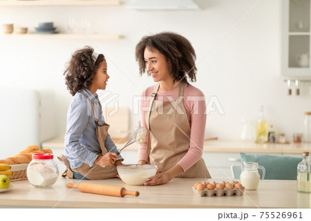 Happy black woman and daughter kneading dough in kitchen Happy black woman and daughter kneading dough in kitchen 75526961