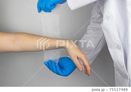 The traumatologist puts a bandage on the forearm of the female patient. The concept of help with fractures and sprains. The technique of applying a cruciform bandage. The traumatologist puts a bandage on the forearm of the female patient. The concept of help with fractures and sprains. The technique of applying a cruciform bandage. 75527489