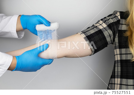 The traumatologist puts a bandage on the elbow of the female patient. The concept of help with fractures and sprains. The technique of applying a cruciform bandage. The traumatologist puts a bandage on the elbow of the female patient. The concept of help with fractures and sprains. The technique of applying a cruciform bandage. 75527551