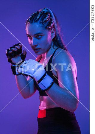 Athletic female MMA fighter posing isolated on blue background in neon light Athletic female MMA fighter posing isolated on blue background in neon light 75527835
