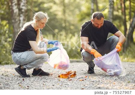 Couple collects garbage in garbage bags in park Couple collects garbage in garbage bags in park 75527907