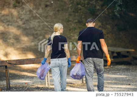 Couple collects garbage in garbage bags in park Couple collects garbage in garbage bags in park 75527943