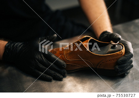 Close-up top view of hands of shoemaker shoemaker wearing black gloves inserts wooden shoe pad into worn light brown leather shoes 75530727
