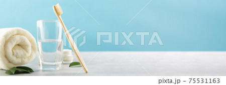 Ecological natural bamboo toothbrush, glass with water, powder for cleaning teeth, towel on a blue background. Sustainable lifestyle concept, zero waste Ecological natural bamboo toothbrush, glass with water, powder for cleaning teeth, towel on a blue background. Sustainable lifestyle concept, zero waste 75531163
