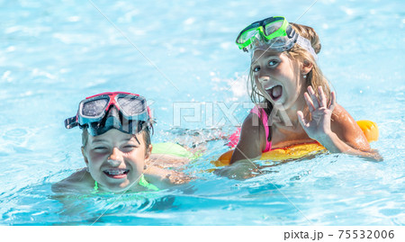 Two female kids having fun inside the pool on a summer day wearing swimming goggles on their foreheads Two female kids having fun inside the pool on a summer day wearing swimming goggles on their foreheads 75532006