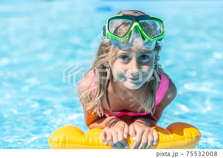 Young girl rests on floating pillow inside the pool with swimming goggles on her forehead, smiling Young girl rests on floating pillow inside the pool with swimming goggles on her forehead, smiling 75532008
