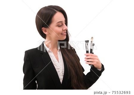 girl with make-up with long dark hair in a business suit holding a brush in his hand, on a white background girl with make-up with long dark hair in a business suit holding a brush in his hand, on a white background 75532693