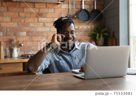 Positive african man answer phone call reading data on laptop 75533081