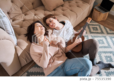 Lesbian woman singing while her girlfriend playing at the ukulele 75535390
