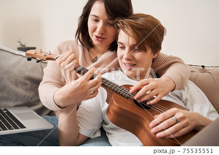 Couple sitting at the sofa and learning how to play at the ukulele 75535551