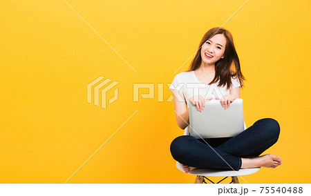 woman teen smiling sitting crossed legs on a chair with laptop computer looking to side 75540488
