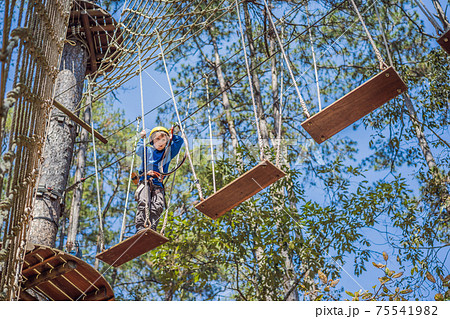 Happy child in a helmet, healthy teenager school boy enjoying activity in a climbing adventure park on a summer day Happy child in a helmet, healthy teenager school boy enjoying activity in a climbing adventure park on a summer day 75541982