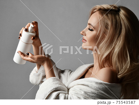Joyful happy blonde woman in bathrobe pours a drop 75543587