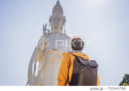Male tourist on the background of Majestic view of the Lady Buddha statue the Bodhisattva of Mercy, Vietnam. White Ladybuddha statue on blue sky background Male tourist on the background of Majestic view of the Lady Buddha statue the Bodhisattva of Mercy, Vietnam. White Ladybuddha statue on blue sky background 75544790