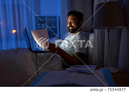 indian man with laptop and papers in bed at night indian man with laptop and papers in bed at night 75544977