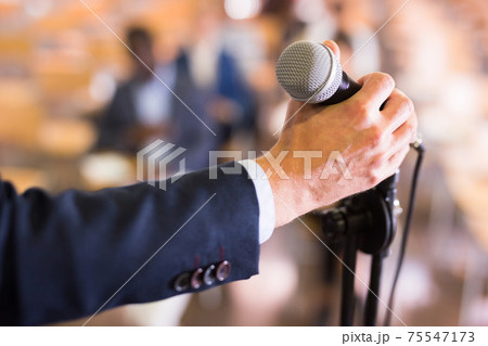 Male hand holding microphone at conference hall 75547173