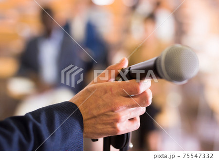 Male hand holding microphone at conference hall 75547332