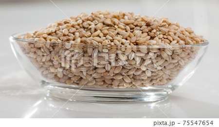 Barley groats in glass bowl on white surface , nobody Barley groats in glass bowl on white surface , nobody 75547654
