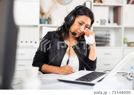 Disappointed female customer support phone operator during work Disappointed female customer support phone operator during work 75548000