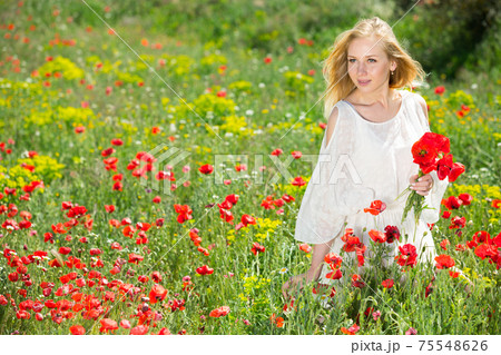 Beautiful young female in white dress holding bouquet of poppy flowers Beautiful young female in white dress holding bouquet of poppy flowers 75548626