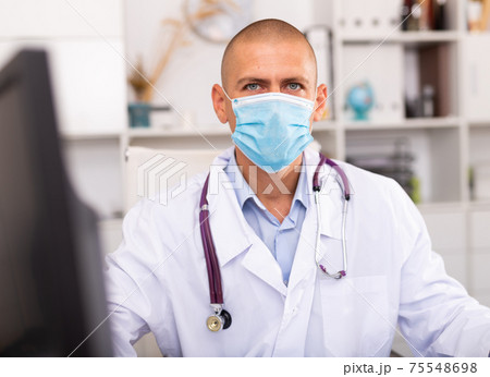 Doctor in protective medical mask sitting at workplace with computer 75548698