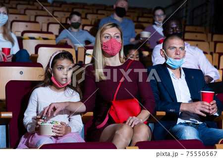 Friendly family in protective masks watching movie in cinema 75550567