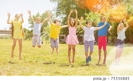 Schoolchildren jumping and smiling together in park Schoolchildren jumping and smiling together in park 75550885