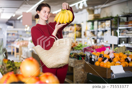 Portrait of smiling young customer selecting bananas in grocery 75553377
