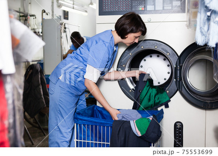 Female worker loading laundry washing machine 75553699