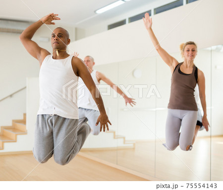 Hispanic man jumping during group choreography in dance studio Hispanic man jumping during group choreography in dance studio 75554143
