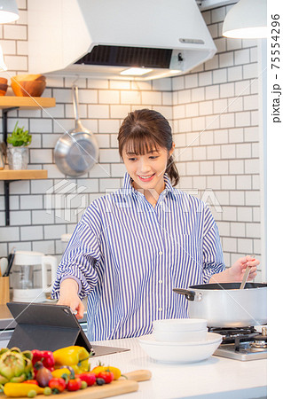 タブレットを見ながら料理する女性 75554296