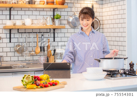 タブレットを見ながら料理する女性 75554301