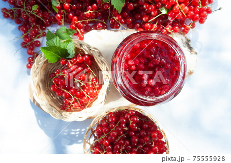 Red and ripe red currants in a straw bowl  and jars of berry jam, flat lay. Harvest and cooking theme 75555928
