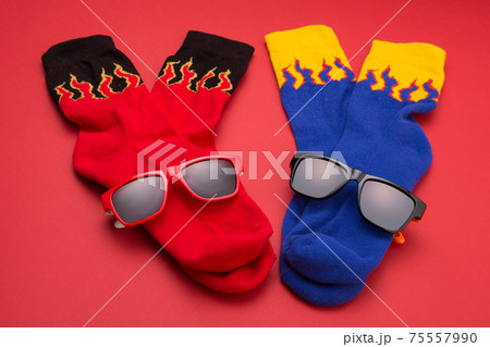 two pairs of colored socks, red and blue, with a flame pattern, lie with sunglasses on a red background 75557990