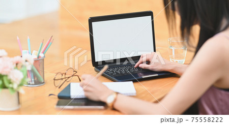 Cropped image woman is using a white blank screen computer laptop at the wooden working desk. Cropped image woman is using a white blank screen computer laptop at the wooden working desk. 75558222