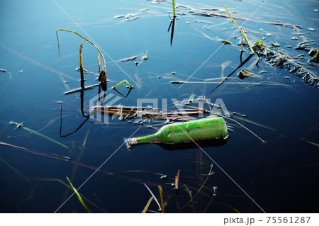 Green glass bottle in blue lake water 75561287