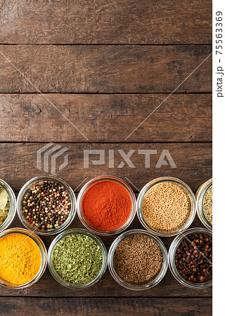 Colourful seasonings in bowls on wooden background with copyspace. Collection of spices 75563369