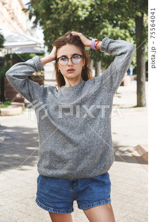 Young woman in gray sweater and denim shorts in the street. 75564041