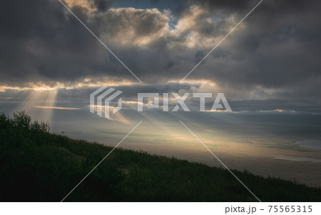Rays of light through the clouds in Panoramic view of Ngorongoro Conservation Area at sunrise from the mountainside. Tanzania, Africa. 75565315