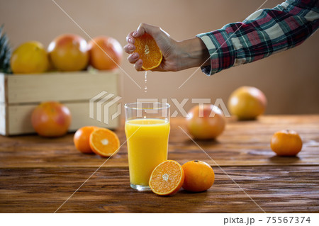 Female hand squeezing fresh orange to the glass on wood table Female hand squeezing fresh orange to the glass on wood table 75567374