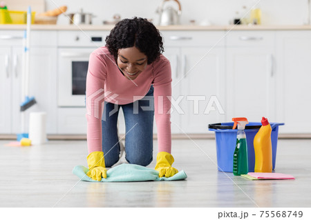 Happy african american young woman cleaning floor in kitchen Happy african american young woman cleaning floor in kitchen 75568749