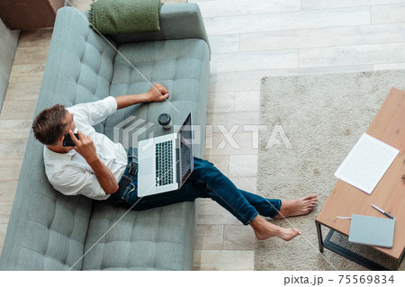 young man is talking on a smartphone, sitting on the sofa. young man is talking on a smartphone, sitting on the sofa. 75569834